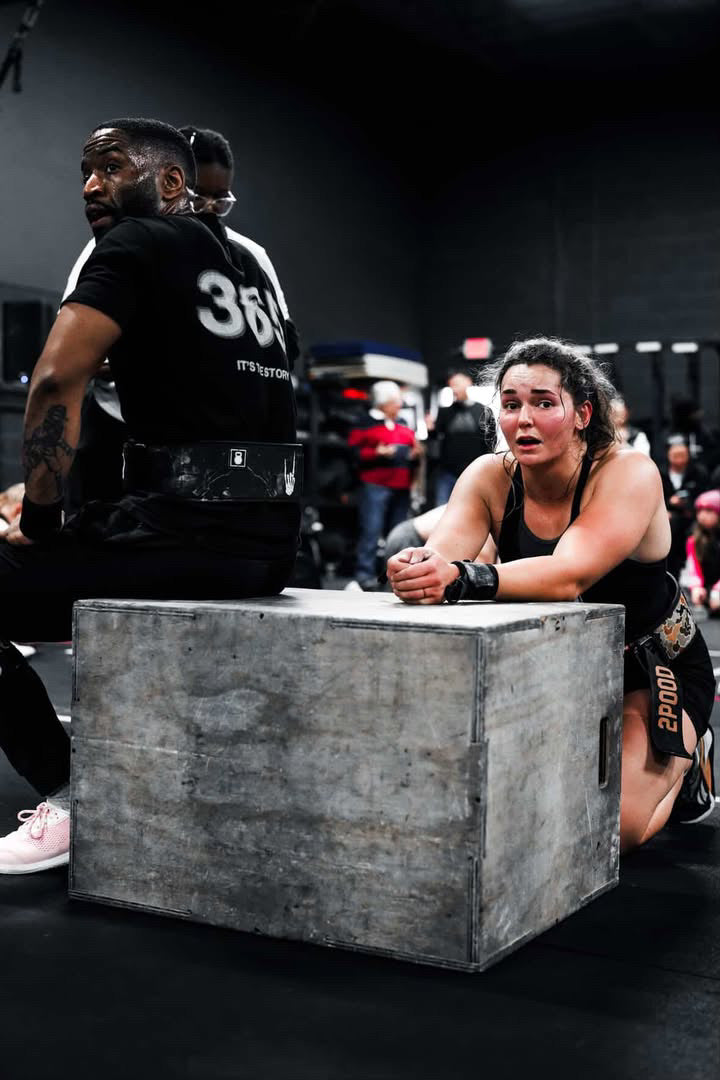 Person lifting a box during a workout with onlookers in the background